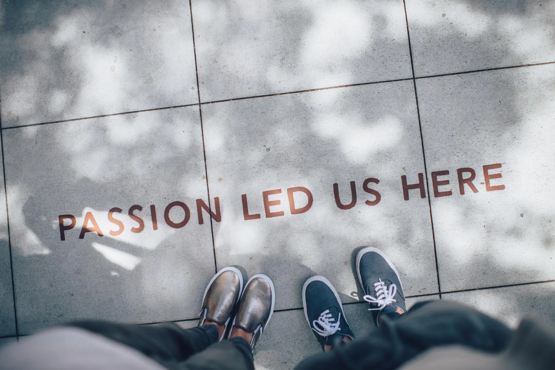 Two pairs of sneakers beside the words Passion Led Us Here on pavement