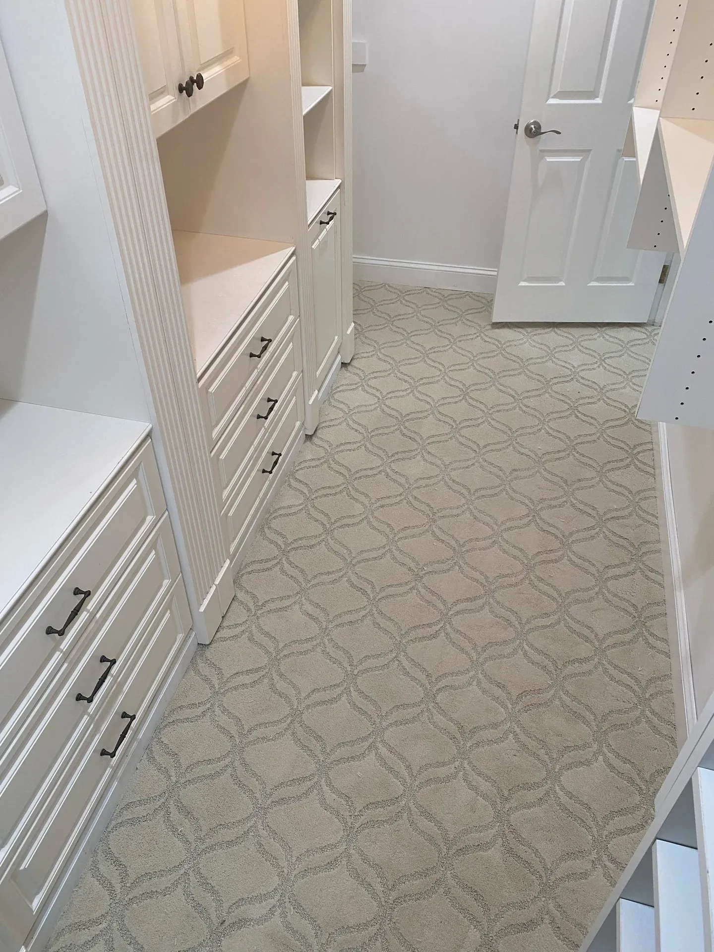 Lattice-pattern carpet in a walk-in closet lined with white built-in cabinets