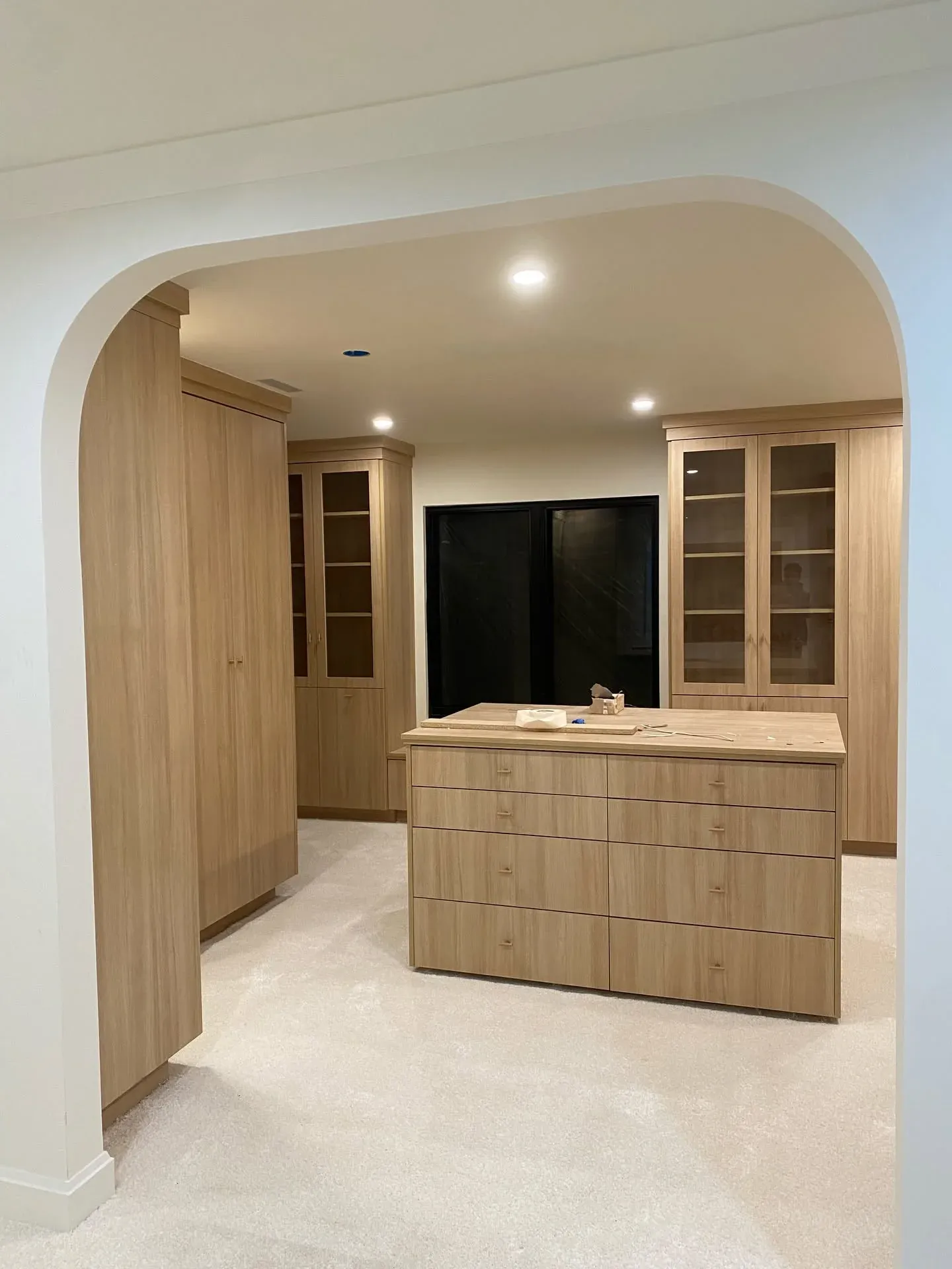 Cream carpet in a walk-in closet with oak cabinetry, seen through an arched doorway