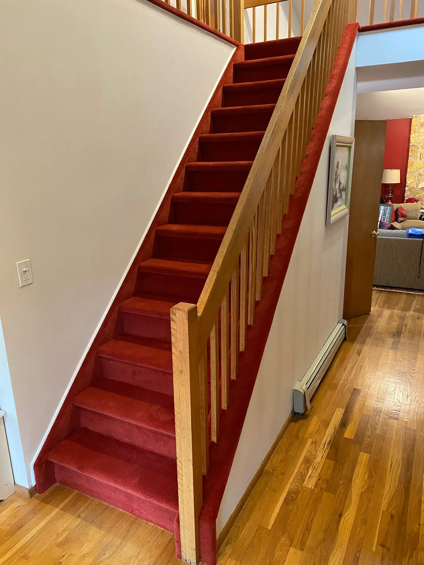 Red carpeted staircase with an oak railing beside a hardwood hallway
